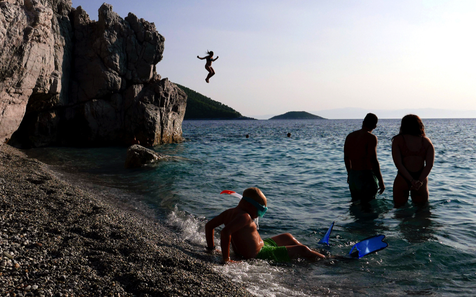 Tourists enjoy the sea at Hovolo beach on the island of Skopelos